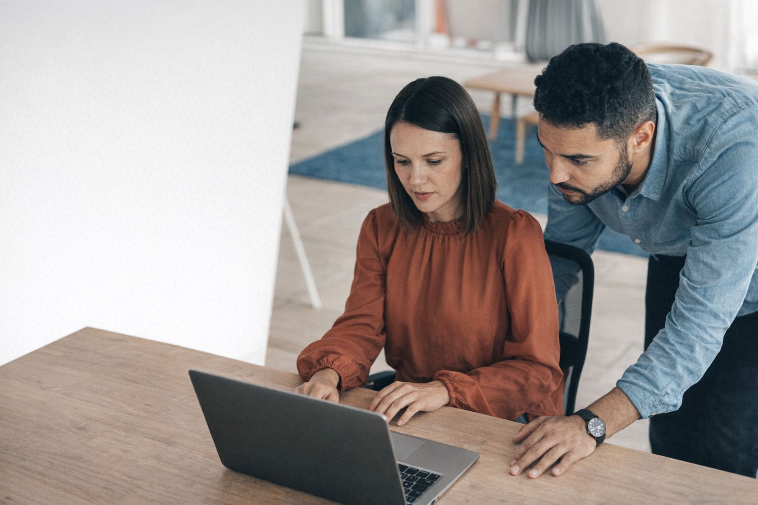 To kolleger kigger koncentreret på en bærbar computer i et kontormiljø.